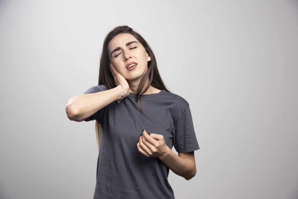 Desvendando os mistérios da DTM: Entenda o que é e como lidar com a Disfunção Temporomandibular 3 mulher jovem em pe e posando sobre um fundo cinza 2